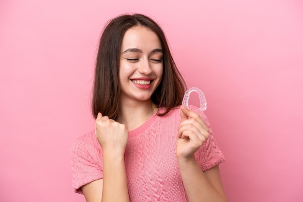 Jonge Oekraïense vrouw met onzichtbare beugels geïsoleerd op roze achtergrond die een overwinning viert