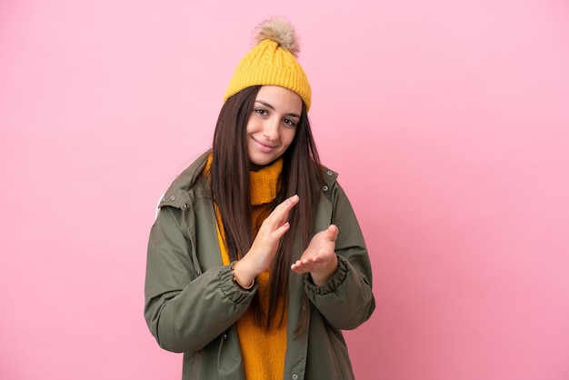 Jonge Oekraïense vrouw met winterjas geïsoleerd op roze achtergrond applaudisseren na presentatie in een conferentie