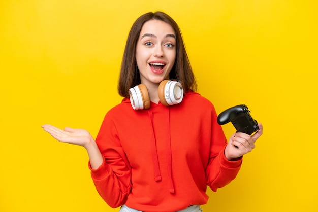 Jonge Oekraïense vrouw speelt met een videogamecontroller geïsoleerd op een gele achtergrond met geschokte gezichtsuitdrukking