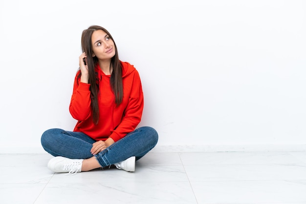 Jonge Oekraïense vrouw zittend op de vloer geïsoleerd op een witte achtergrond denken een idee