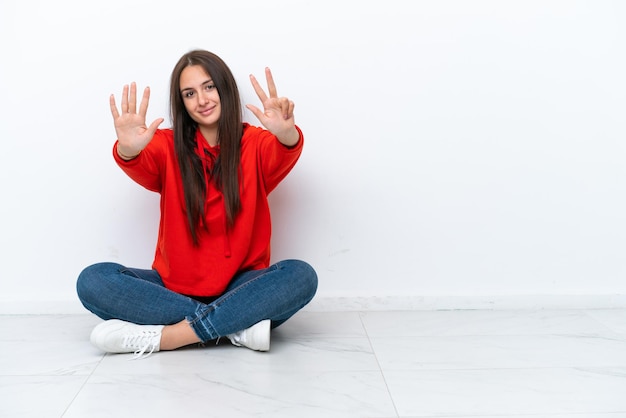 Jonge Oekraïense vrouw zittend op de vloer geïsoleerd op een witte achtergrond telt acht met vingers