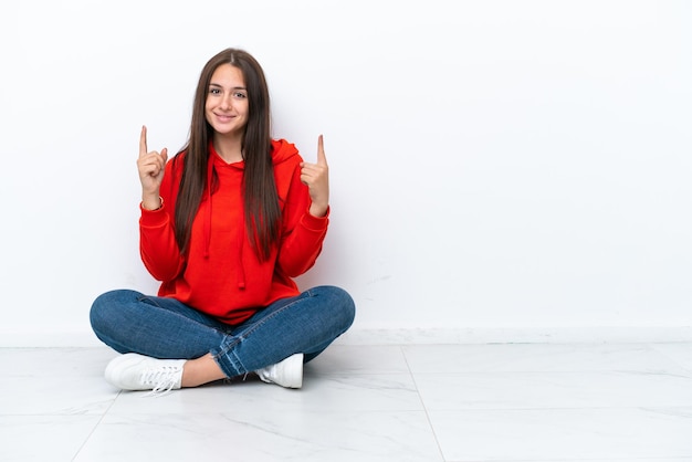 Jonge Oekraïense vrouw zittend op de vloer geïsoleerd op een witte achtergrond wijzend op een geweldig idee