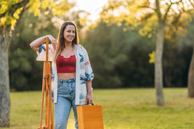 Jonge oman staat met een houten aktetas en een canvas in een park