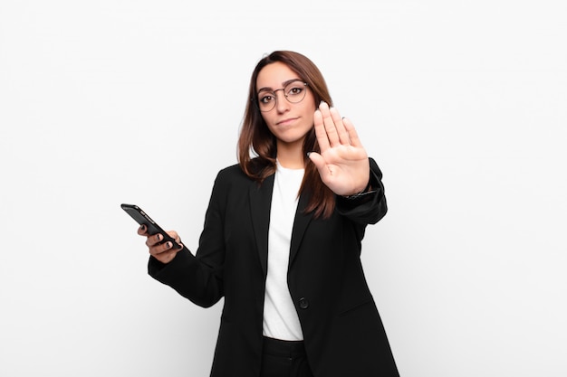 Jonge onderneemster die ernstig, streng, ontstemd en boos kijken die open palm tonen die eindegebaar maken en een mobiele telefoon houden