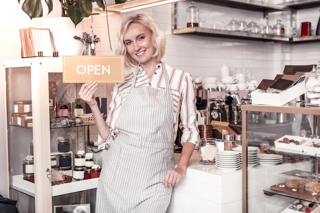 Jonge ondernemer. Blije positieve vrouw die naar u glimlacht tijdens het openen van haar café