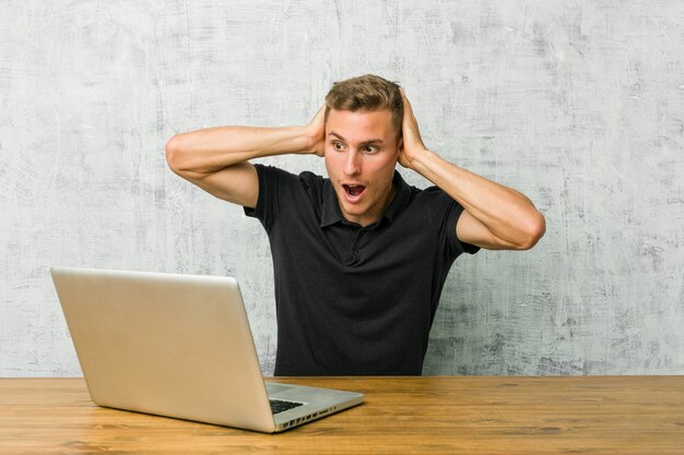 Jonge ondernemer die met zijn laptop aan een bureau werkt dat oren behandelt met handen die niet te hard geluid proberen te horen