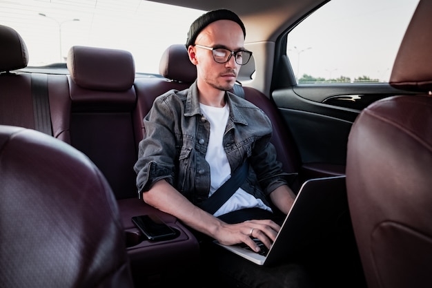 Jonge ondernemer met behulp van laptop op een achterbank van een auto.