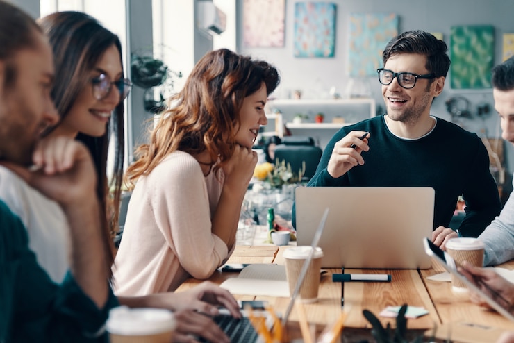 Foto jonge ondernemers. groep jonge moderne mensen in slimme vrijetijdskleding die iets bespreken en glimlachen terwijl ze in het creatieve kantoor werken