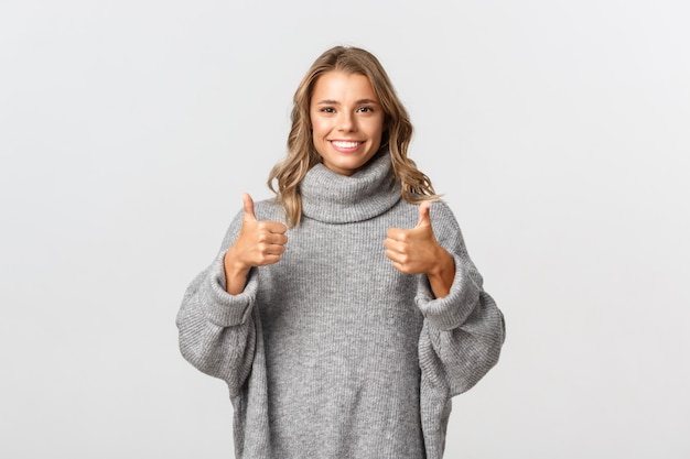 Jonge ondersteunende vrouw met blond kort haar, die thumbs-up toont en glimlacht, als iets of geef