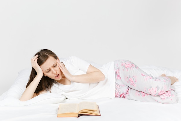 Jonge ontevreden vrouw liggend in bed met wit laken, kussen, deken op witte muur