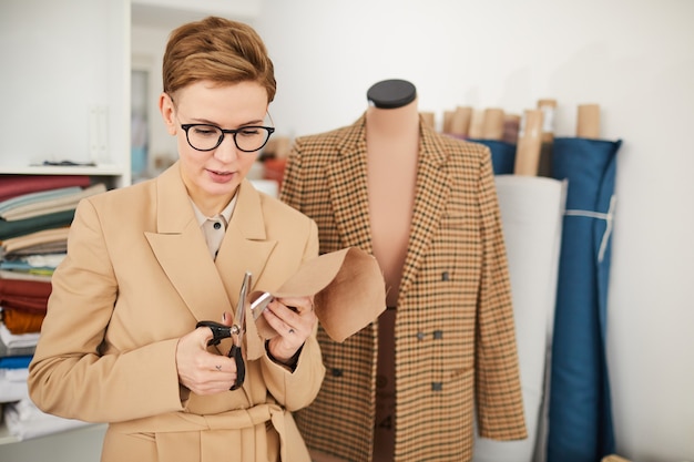 Jonge ontwerper in brillen permanent en stuk stof knippen met een schaar in de werkplaats