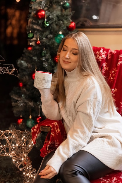 Jonge openhartige vrouw in gebreide gezellige trui in handen kopje cacaodrank met marshmallow zittend ontspannen op stoel camping buiten en plezier gelukkig nieuwjaar en prettige kerstvakantie vooravond