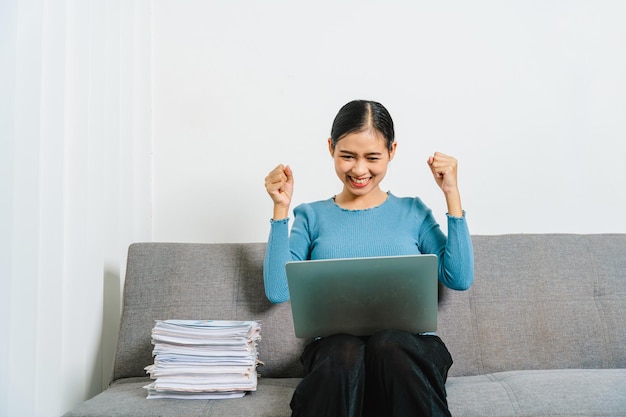 Jonge opgewonden Aziatische vrouw die op de bank zit en online viert win succes prestatie resultaat blij bij het lezen van goed nieuws e-mail