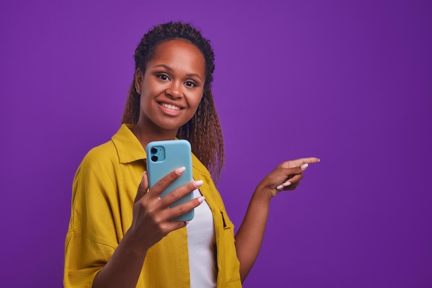 Jonge optimistische afro-amerikaanse vrouw houdt de telefoon vast met een glimlach en wijst terug