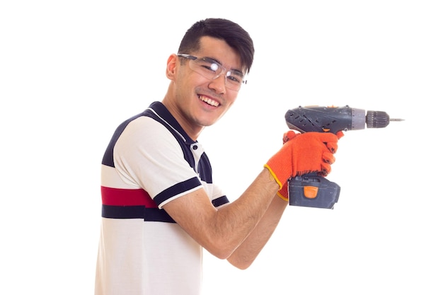 Jonge optimistische man met oranje handschoenen en beschermende bril met grijze elektrische schroevendraaier