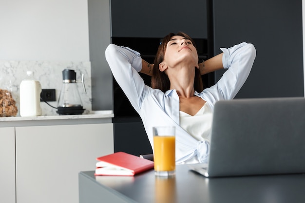 jonge optimistische positieve vrouw binnenshuis thuis in de keuken met behulp van laptopcomputer rust ontspannen.