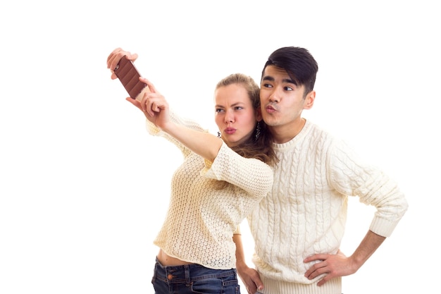 Jonge optimistische vrouw met jonge man met donker haar in witte truien en jeans die selfie maken