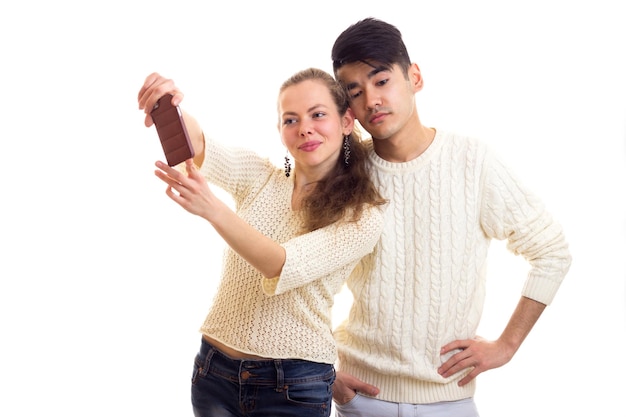 Jonge optimistische vrouw met jonge man met donker haar in witte truien en jeans die selfie maken