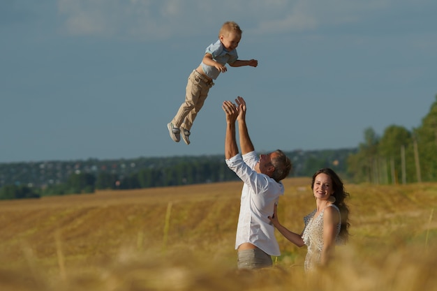 Jonge ouders en kind lopen door een tarweveld. moeder, vader en kleine jongen ontspannen samen buiten. familie op zomerweide