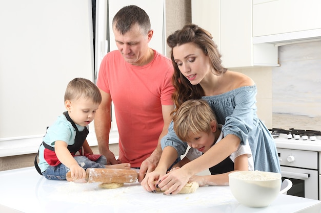 Jonge ouders helpen jonge zoons het deeg op de keukentafel te kneden