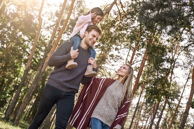 Jonge ouders met dochtertje in herfst bos. Vader houdt meisje vast, moeder loopt in de buurt en raakt haar hand aan