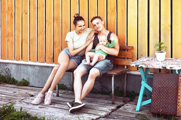 Jonge ouders van jaren met een zes maanden oud kind in hun armen zitten in de achtertuin van hun huis.