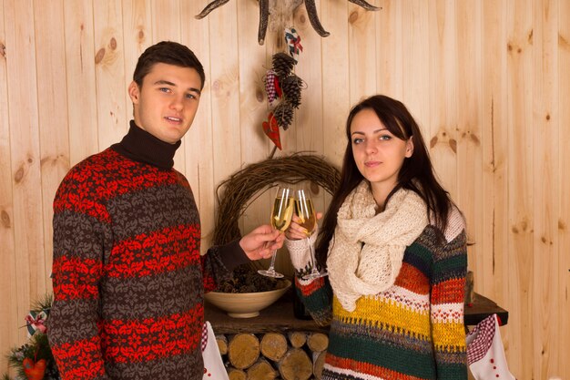 Jonge partners in casual winteroutfits die fluitglazen champagne in huis gooien terwijl ze naar de camera kijken.