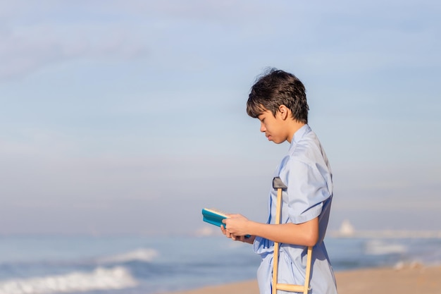 Jonge patiënten met krukken die een boek lezen op het strand, gehandicapte man met krukken tijdens het reizen op het strand.