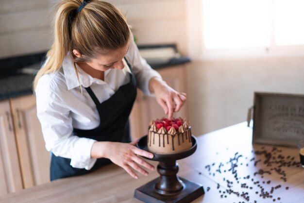 Jonge patissier die een heerlijke zelfgemaakte chocoladetaart met fruit in de keuken kookt