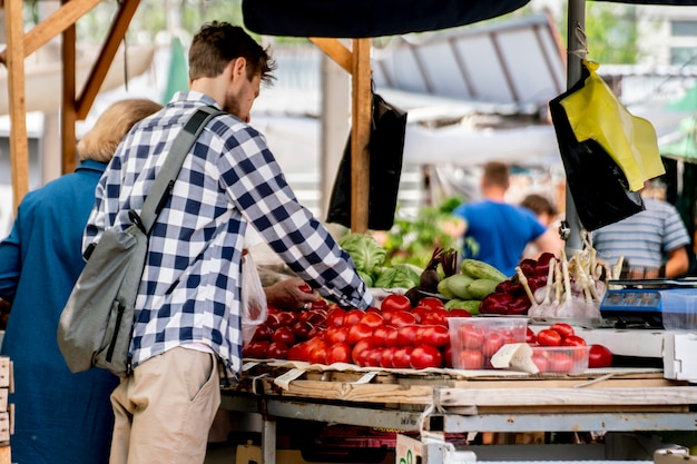 Jonge pesron kiest verse rijpe groenten op de buitenmarkt en koopt deze