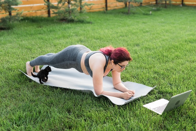 Foto jonge plus-maatvrouw in sportieve top en legging die in plank op yogamat staat en tijd doorbrengt met