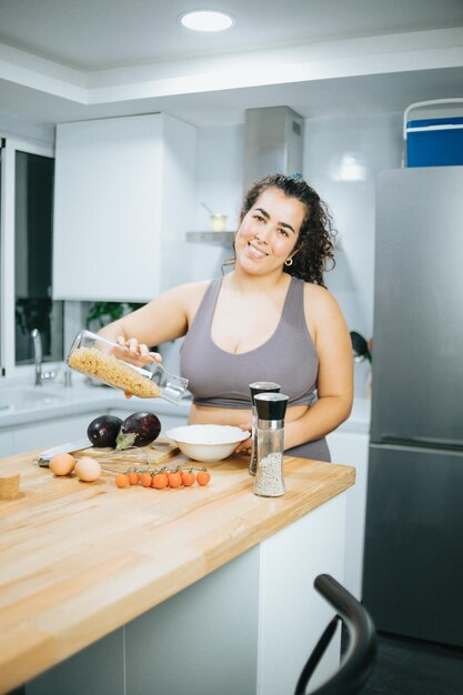 Jonge plus-size vrouw die gezond voedsel kookt na een training met low carb-producten in een moderne keuken Kopieer de ruimtebeeldtraining thuis om voor de zomer af te vallen