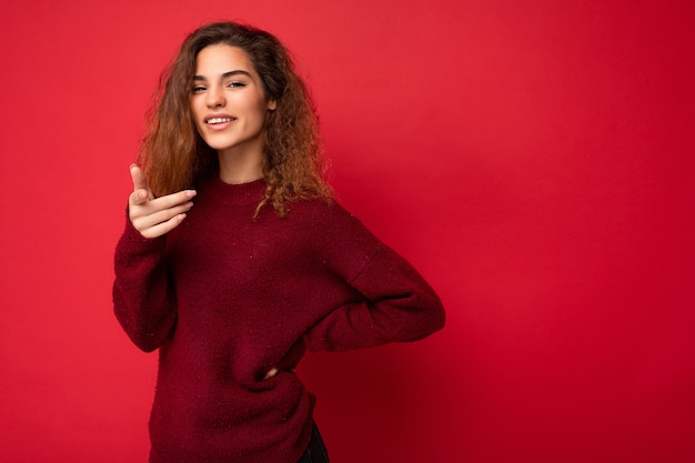 Jonge positieve, gelukkige, mooie brunette krullende vrouw met oprechte emoties die casual rood draagt