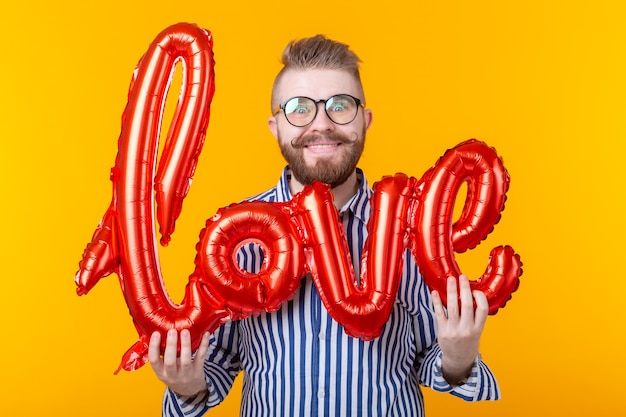 Jonge positieve hipster man met een opblaasbare liefde inscriptie in zijn handen op een gele muur. Het concept van felicitaties van zijn soulmate.