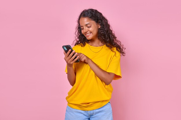 Jonge positieve Indiase vrouw tiener met telefoon in handen staat in roze studio