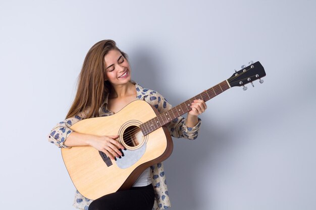 Jonge positieve vrouw met lang haar in bruine jas gitaar spelen in studio