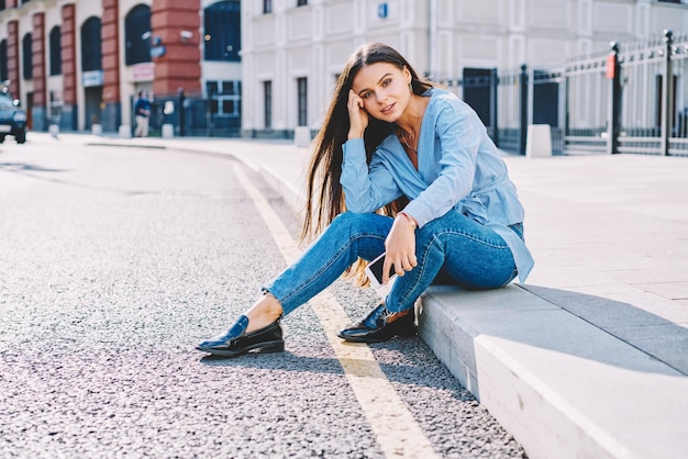 Foto jonge prachtige vrouw in mode kleding zittend op straat charmante hipster meisje in denim jeans