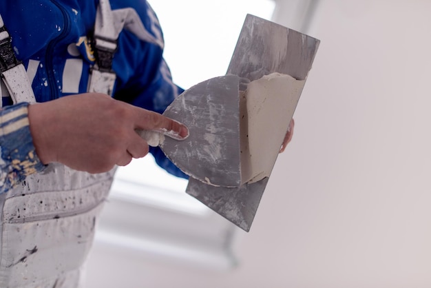 Foto jonge professionele bouwvakker die op gipsmuren pleistert in het nieuwe grote moderne appartement met twee verdiepingen