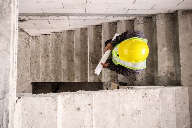 Jonge professionele ingenieur werknemer in beschermende helm en blauwdrukken papier bij de hand op de bouwplaats van het huis