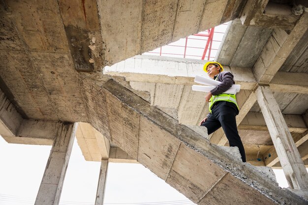 Jonge professionele ingenieur werknemer in beschermende helm en blauwdrukken papier bij de hand op de bouwplaats van het huis