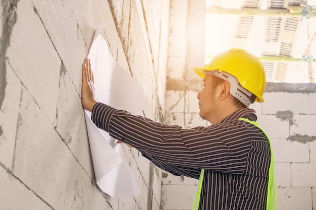 Jonge professionele ingenieur werknemer in beschermende helm werken bij woningbouw bouwplaats met blauwdruk