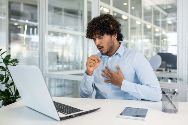 Jonge professionele man die hoest terwijl hij op de laptop werkt in het kantoor