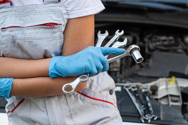 Jonge professionele vrouwelijke monteur inspecteert onder de motorkap van een auto