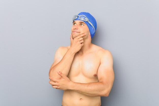 Jonge professionele zwemmersmens die zijdelings met twijfelachtige en sceptische uitdrukking kijkt.