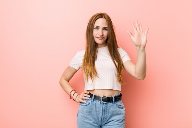 Jonge redhead gembervrouw tegen een roze muur die vrolijk tonend nummer vijf met vingers glimlachen.