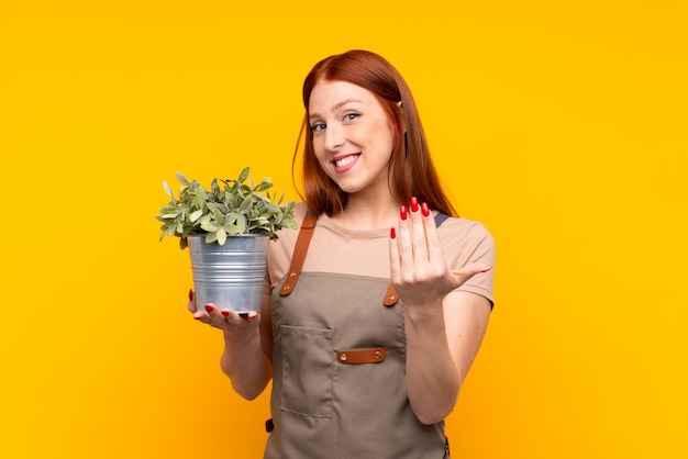 Jonge redhead tuinmanvrouw die een installatie over geïsoleerde gele muur houden die uitnodigen te komen