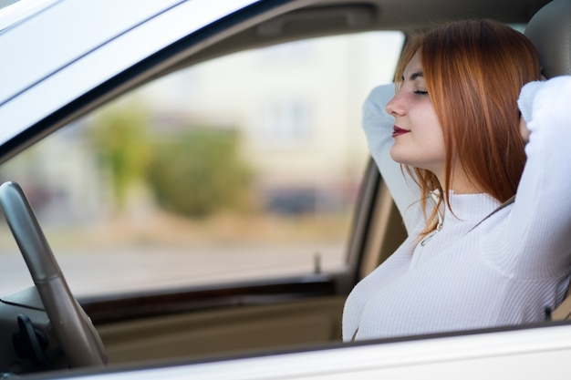 Jonge redhead vrouwenbestuurder die door veiligheidsgordel wordt vastgemaakt die in een auto rust die gelukkig glimlacht.