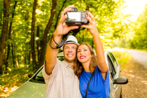 Jonge reizigers staan voor een auto in het bos en nemen een foto van zichzelf.