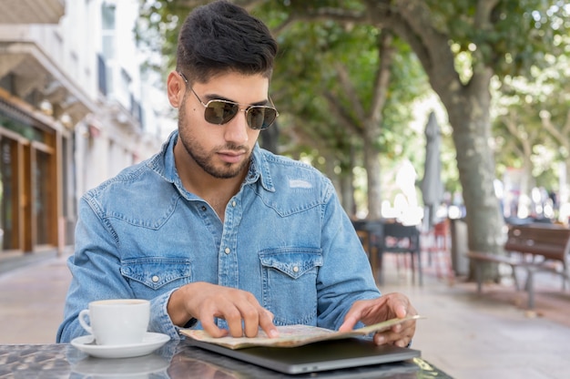 Jonge reizigersman zit op een caféterras en plant haar reis met kaart en laptop