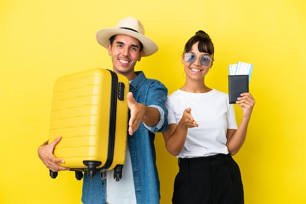 Jonge reizigersvrienden die een koffer en een paspoort houden dat op gele achtergrond wordt geïsoleerd en handen schudden voor het sluiten van een goede deal